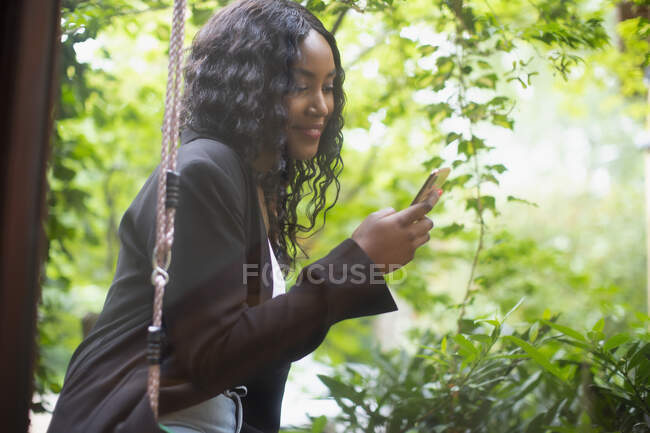 Молода жінка використовує смартфон на гойдалці на патіо — стокове фото