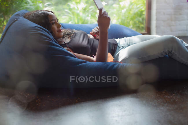 Mulher jovem relaxando usando tablet digital em cadeira de beanbag — Fotografia de Stock