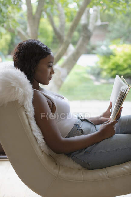Libro de lectura relajante de la joven mujer en el salón - foto de stock