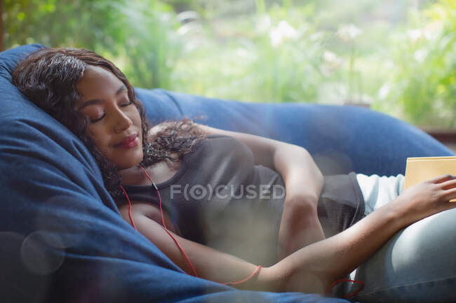 Serene young woman with headphones listening to music in beanbag chair — Stock Photo