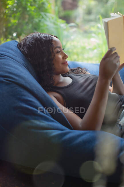 Молода жінка розслабляє читання книги в кріслі для мішків — стокове фото