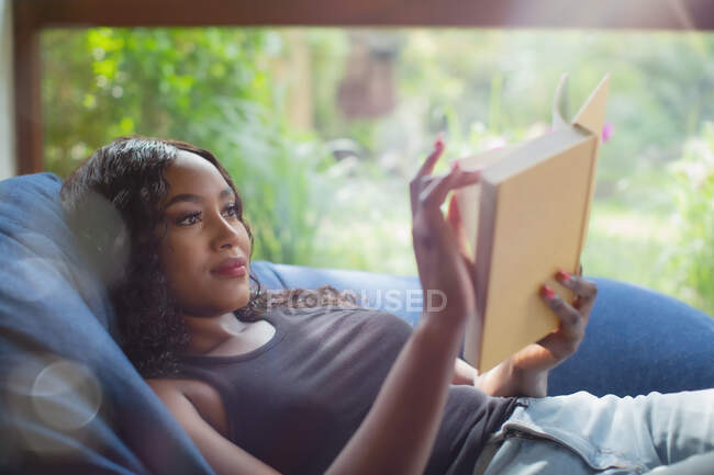Young woman relaxing reading book in beanbag chair — Stock Photo