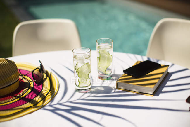 Acqua di cetriolo e prenotare sulla soleggiata tavola a bordo piscina estiva — Foto stock