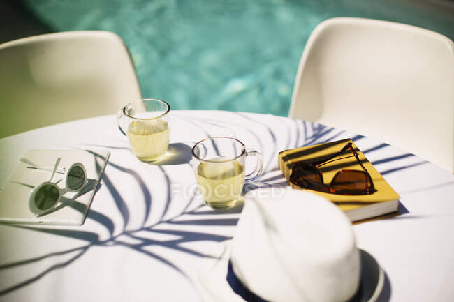 Té y gafas de sol en la soleada mesa junto a la piscina - foto de stock