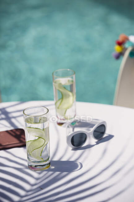 Acqua di cetriolo e occhiali da sole sul soleggiato tavolo patio a bordo piscina — Foto stock