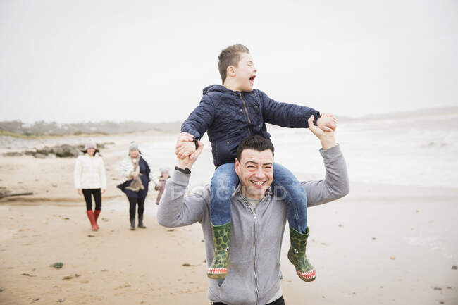 Feliz padre llevando a su hijo con Síndrome de Down en hombros en la playa - foto de stock