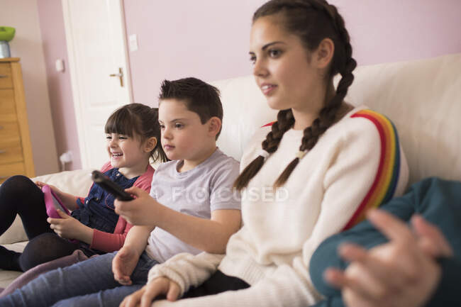 Мальчик с синдромом Дауна смотрит телевизор с братьями и сестрами на диване — стоковое фото