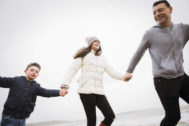 Niño feliz con síndrome de Down corriendo en la playa con el padre y la hermana - foto de stock
