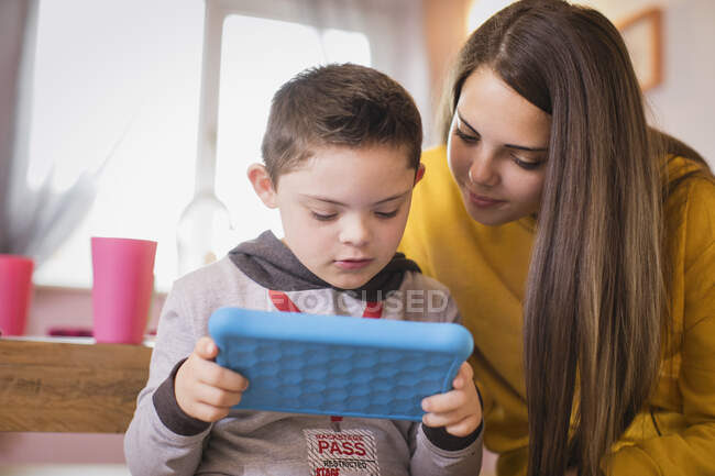Mädchen beobachtet Bruder mit Down-Syndrom mit digitalem Tablet — Stockfoto