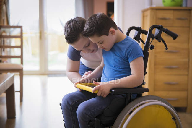 Niño con Síndrome de Down usando tableta digital en silla de ruedas - foto de stock