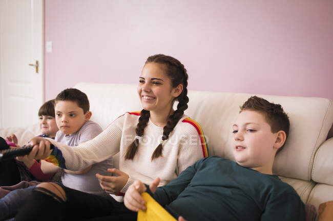 Fille heureuse regardant la télévision avec des frères et sœurs sur le canapé — Photo de stock