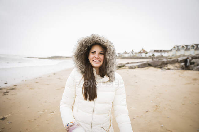 Portrait happy carefree teenage girl in fur jacket on ocean beach — Stock Photo
