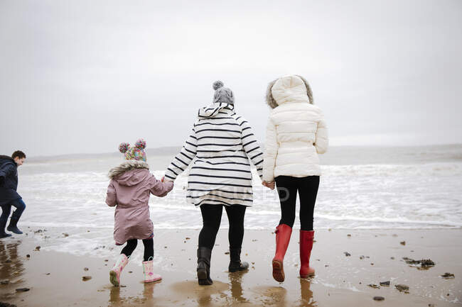 Family in warm clothing walking on winter ocean beach — Stock Photo