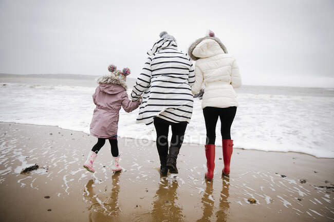 Mother and daughters in warm clothing walking on winter ocean beach — Stock Photo