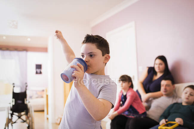 Мальчик с синдромом Дауна пьет и ликует в гостиной — стоковое фото