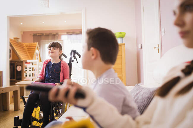 Menina feliz em cadeira de rodas com irmãos em casa — Fotografia de Stock