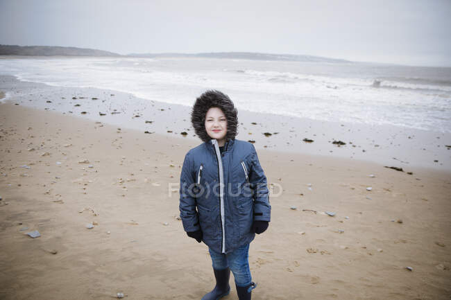 Portrait confident boy in fur hooded jacket on winter ocean beach — Stock Photo
