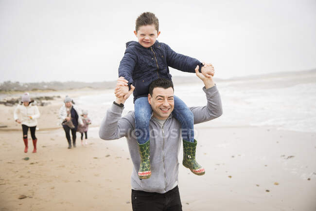 Retrato juguetón padre llevando hijo en hombros en la playa de invierno - foto de stock