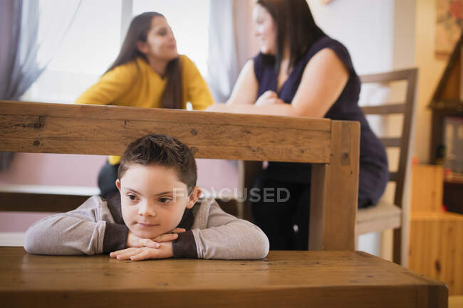 Niño con síndrome de Down jugando debajo de la mesa de comedor - foto de stock
