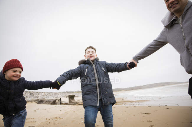 Playful father and sons holding hands on winter ocean beach — Stock Photo