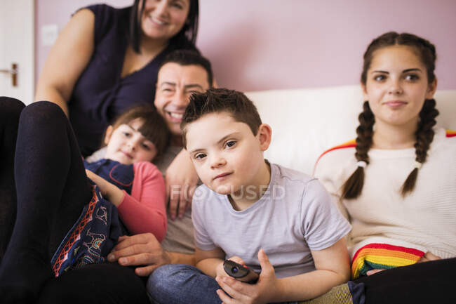 Retrato menino com Síndrome de Down assistindo TV com a família no sofá — Fotografia de Stock