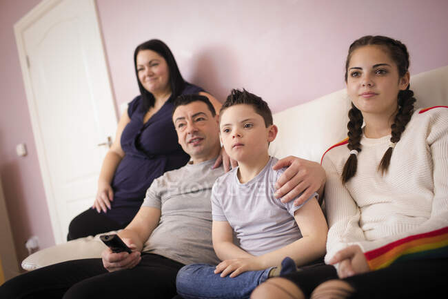 Famille avec trisomie 21 fils regardant la télévision sur le canapé du salon — Photo de stock