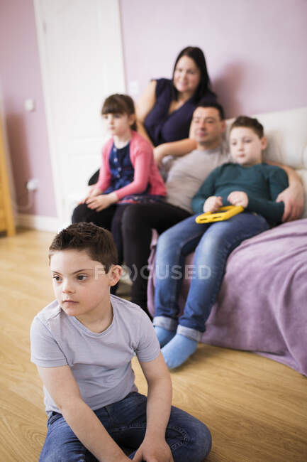 Мальчик с синдромом Дауна смотрит телевизор с семьей в гостиной — стоковое фото