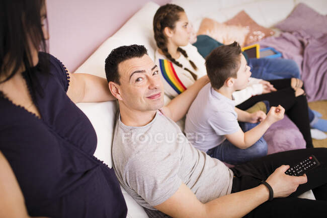Retrato hombre feliz viendo la televisión en el sofá con la familia - foto de stock