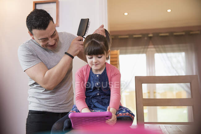 Père brossage des cheveux de la fille en utilisant une tablette numérique — Photo de stock