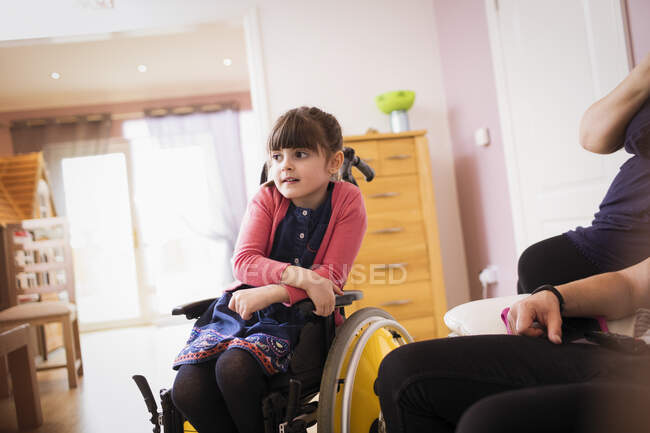 Дівчина в інвалідному візку дивиться телевізор у вітальні — стокове фото
