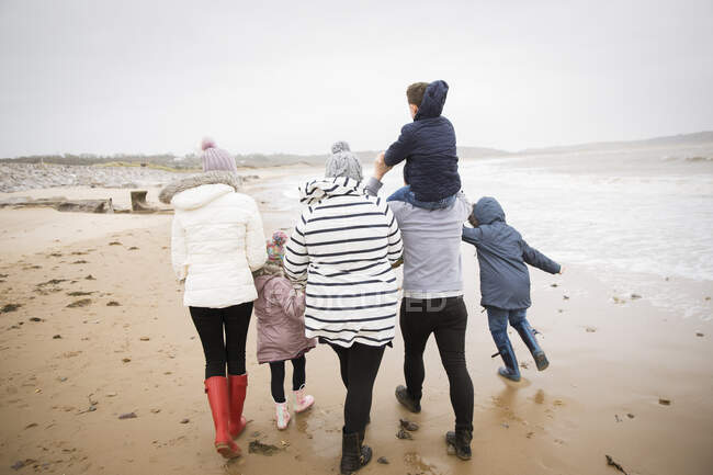 Family in warm clothing walking on winter ocean beach — Stock Photo