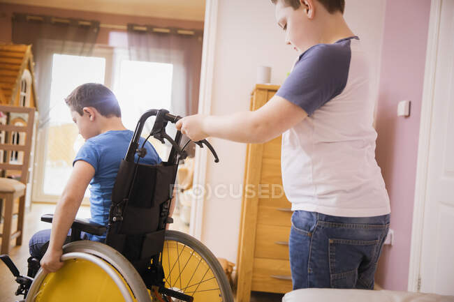 Garçon poussant frère en fauteuil roulant — Photo de stock