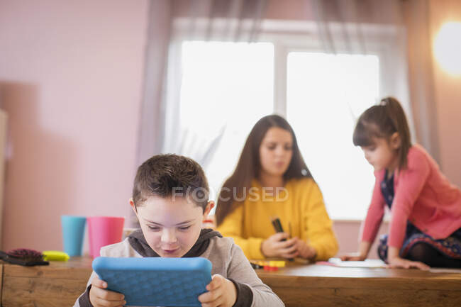 Хлопчик з синдромом Дауна використовує цифровий планшет за обіднім столом — стокове фото