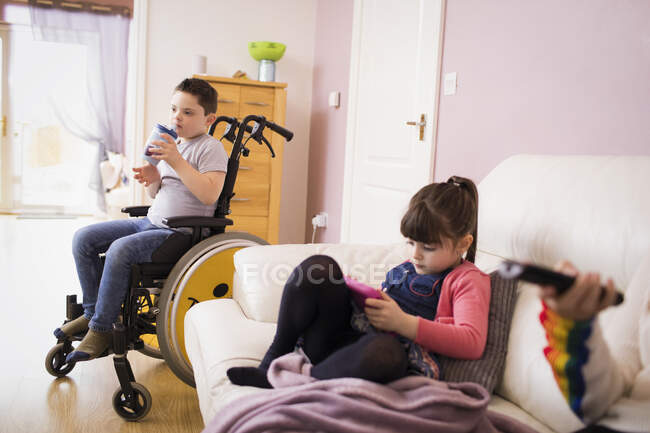 Menino com Síndrome de Down em cadeira de rodas e irmã na sala de estar — Fotografia de Stock