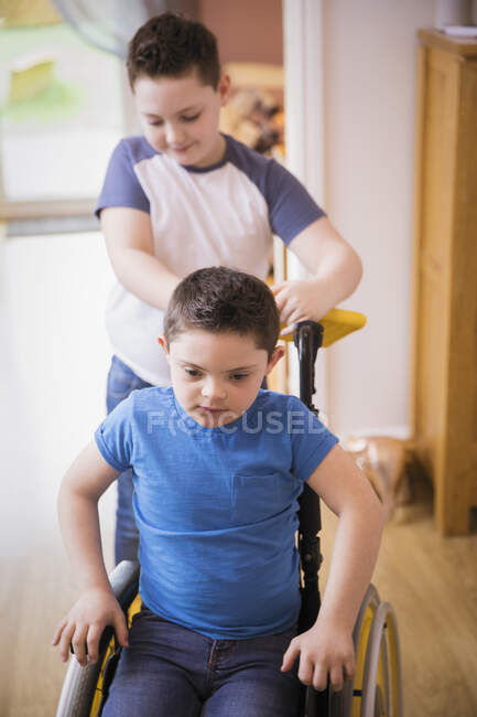 Garçon poussant frère avec trisomie 21 en fauteuil roulant — Photo de stock