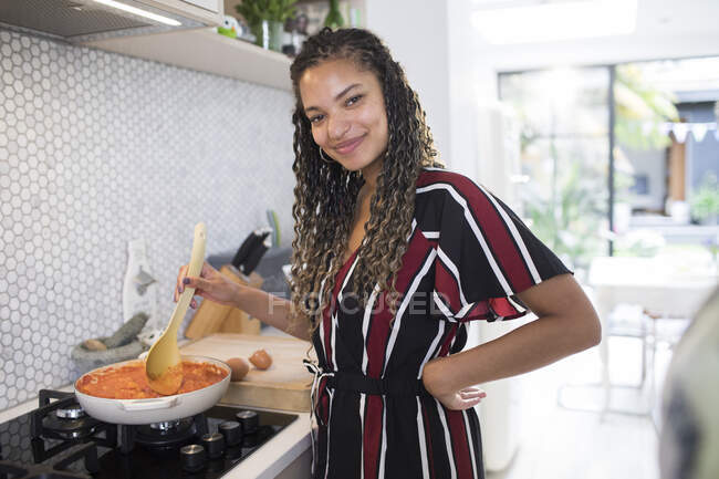 Portrait happy young woman cooking at stove in kitchen — Stock Photo