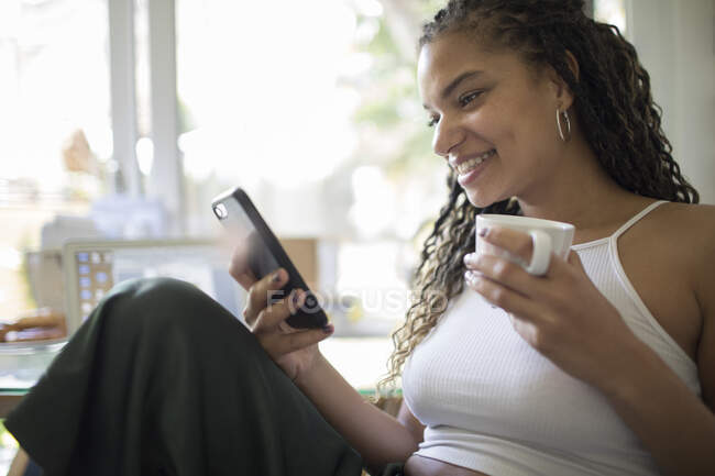 Молода жінка п'є каву і використовує смартфон — стокове фото