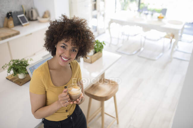 Portrait happy young woman drinking cappuccino in kitchen — Stock Photo