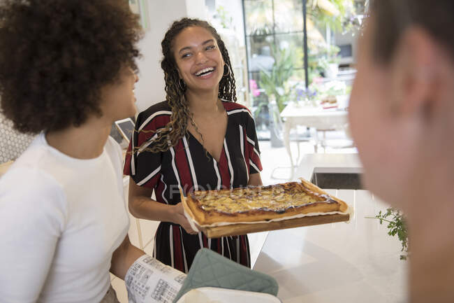Happy young woman serving homemade pizza to friends in kitchen — Stock Photo