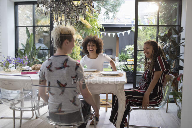 Amigos jóvenes felices en una mesa de comedor soleada - foto de stock