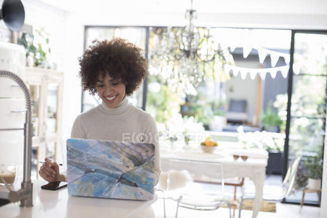 Sorridente giovane donna freelance che lavora al computer portatile in cucina — Foto stock