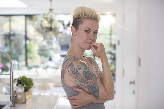 Retrato mujer confiada con tatuajes en la cocina - foto de stock