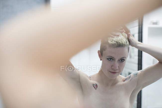 Femme avec tatouages fixant les cheveux dans la salle de bain — Photo de stock