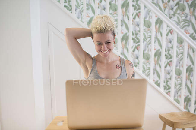 Happy woman with tattoos working at laptop in kitchen — Stock Photo