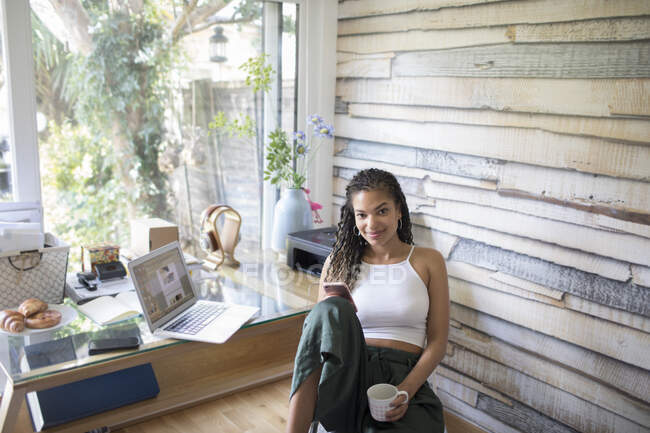 Портрет уверенной в себе молодой женщины с помощью смартфона в домашнем офисе — стоковое фото