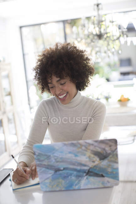 Smiling young female freelancer working at laptop in kitchen — Stock Photo