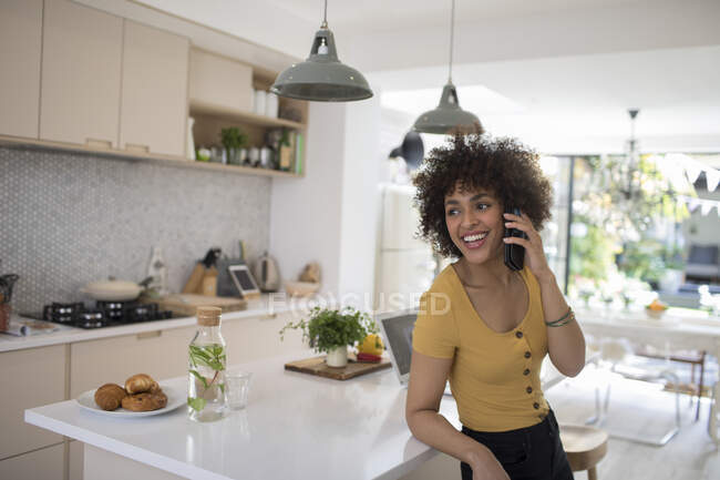 Щаслива молода жінка розмовляє на смартфоні на кухні — стокове фото