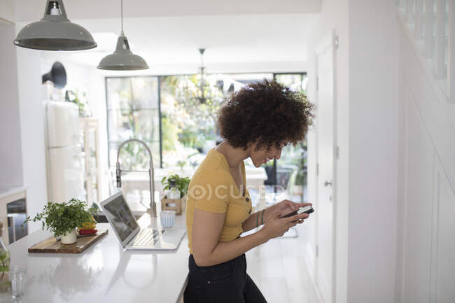 Mulher jovem textando com telefone inteligente na cozinha — Fotografia de Stock