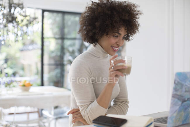 Jeune femme indépendante buvant du café sur un ordinateur portable — Photo de stock