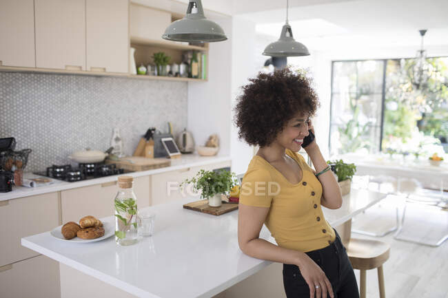 Sorrindo jovem mulher falando no telefone inteligente na cozinha — Fotografia de Stock